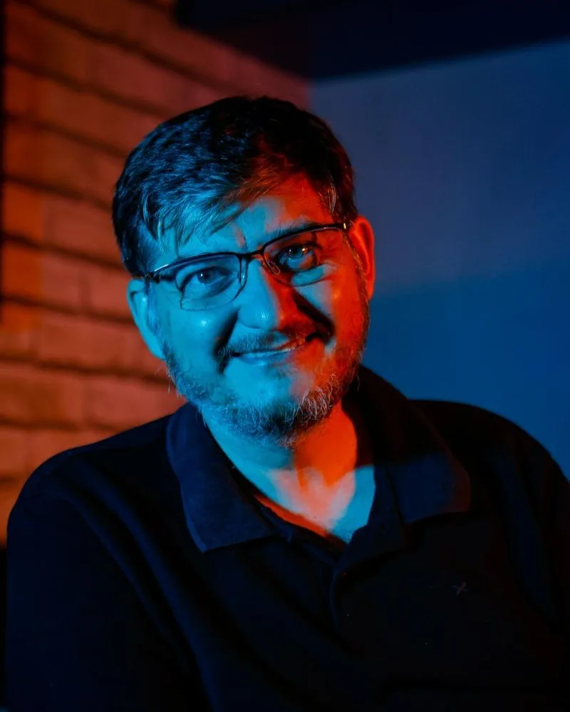 Retrato de Aislan Greca, sorrindo, em luz azul e laranja
